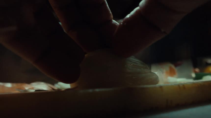 Close-up slow motion shot from a low angle shows a chef slicing a white onion on a wooden cutting board