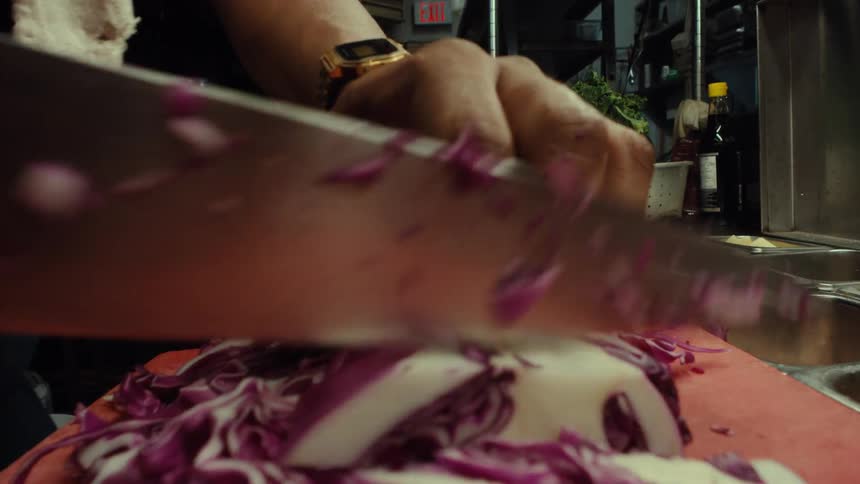 A dynamic close-up shot reveals a chef's hands skillfully and rapidly chopping red cabbage in a professional kitchen