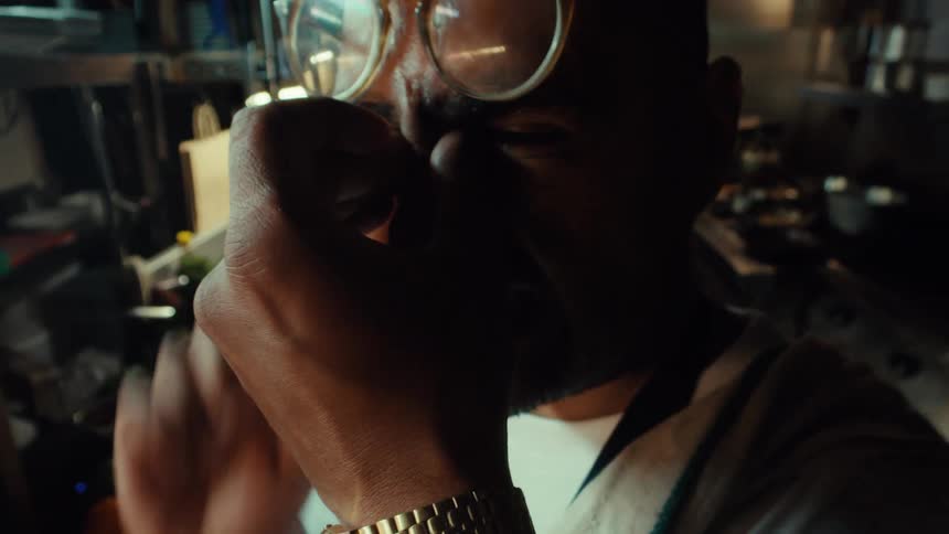 A tired male chef with glasses rubs his eyes, feeling stressed and exhausted in a dimly lit professional kitchen