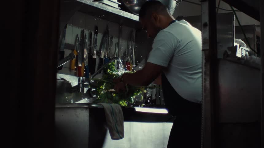 Slow-motion shot of a chef carefully washing fresh leafy greens in a professional kitchen sink