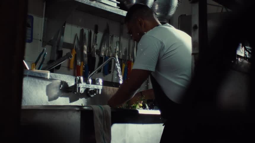 A chef meticulously washes fresh greens in a commercial kitchen sink in dramatic slow motion