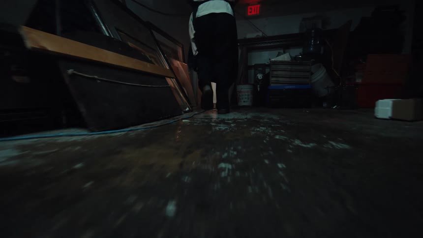 A low-angle dolly shot follows a worker as they walk through a dark and grimy restaurant basement