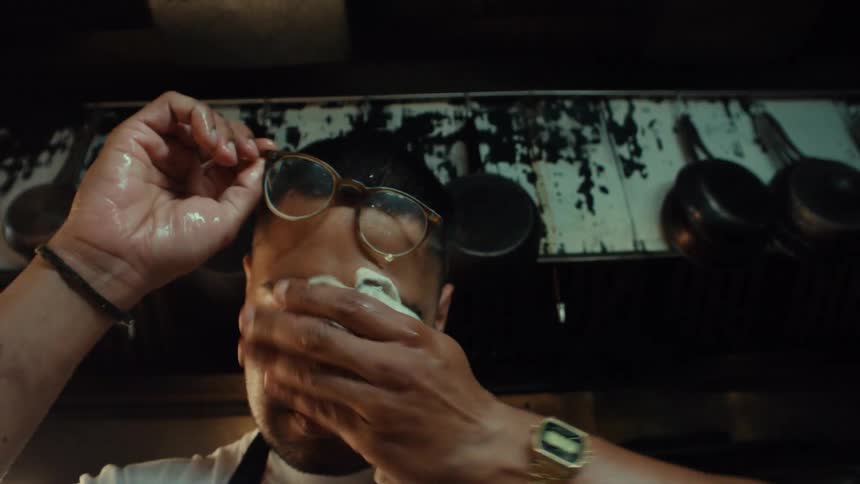A tired and sweaty chef wipes his brow in a hot restaurant kitchen in slow motion