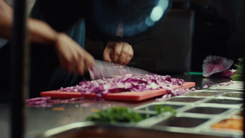 A chef in an apron skillfully chops red cabbage on a cutting board in a commercial kitchen