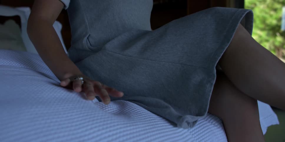 A woman folds her legs sitting on a white bed