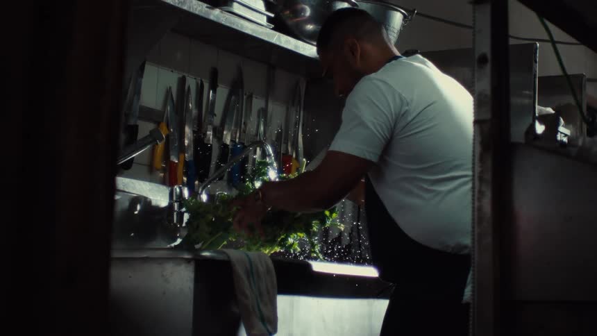 A chef carefully washes fresh greens under running water in a professional kitchen in slow motion