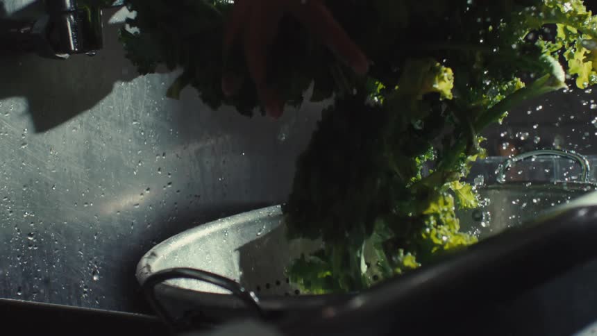 A chef carefully rinses a bunch of fresh kale in a restaurant kitchen sink in dramatic slow motion