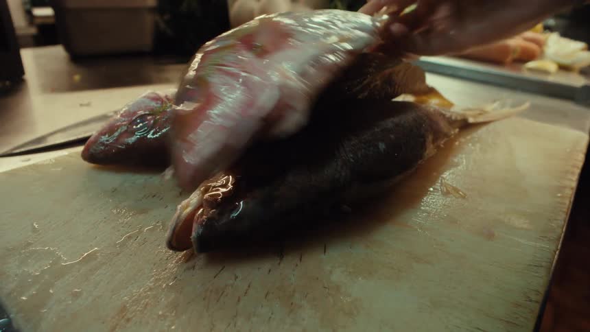 A chef places several fresh whole red fish onto a wooden cutting board in a kitchen