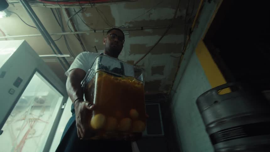 A strong chef carries a heavy container of brining eggs out of a walk-in refrigerator in slow motion