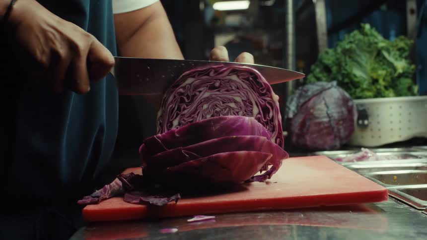 A chef's hands carefully slice a fresh red cabbage on a cutting board in a professional kitchen