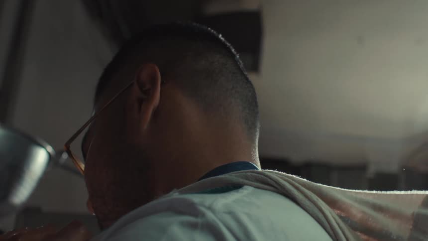 An exhausted chef wipes sweat from his face with a towel while working in a hot kitchen