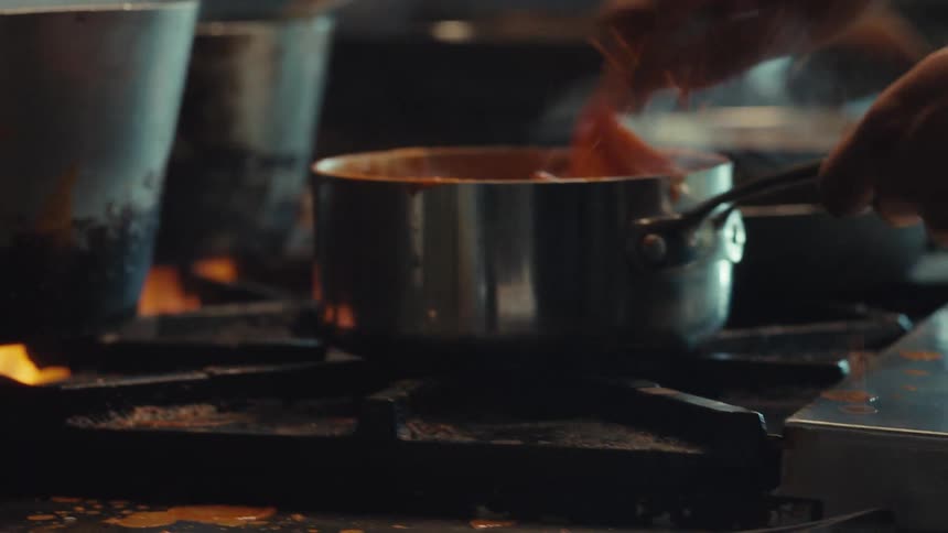 A chef vigorously stirs a simmering red sauce in a pot on a professional restaurant stove