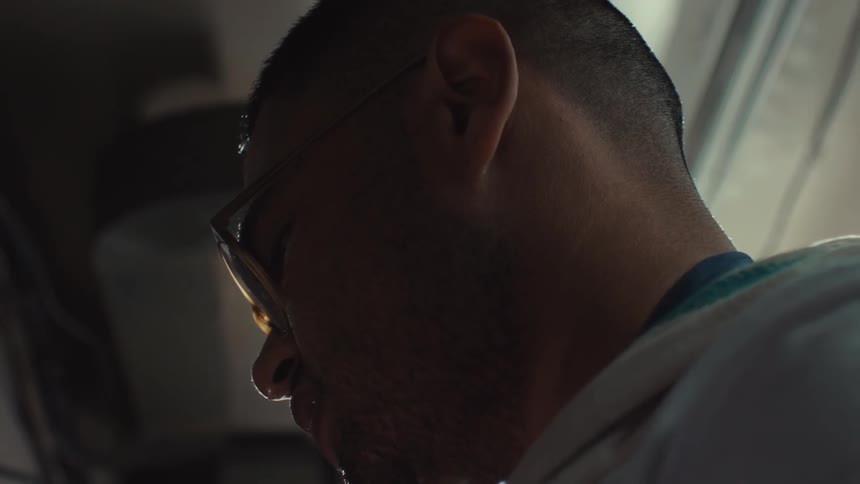 Close-up slow motion shot of a colleague's hand wiping the sweat from a focused chef working in a hot, professional kitchen