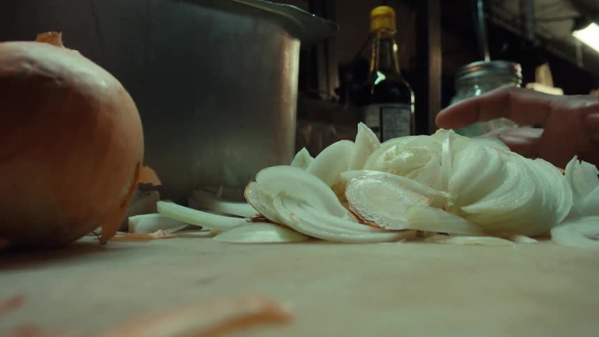 Slow motion macro shot of a chef's hands gathering freshly sliced white onions from a cutting board in a professional kitchen