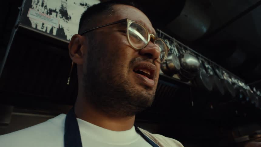 Low-angle close-up of a chef grimacing in pain as he sucks on his bloody finger after an accident in the kitchen