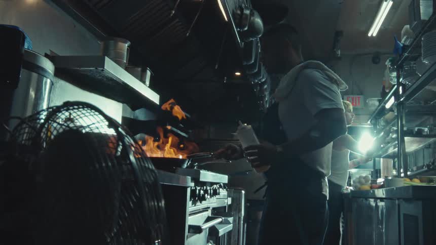 A professional chef skillfully cooks with a large open flame in a restaurant kitchen in dramatic slow motion