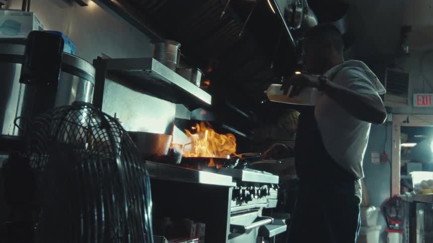 Slow motion shot of a professional chef creating a large, dramatic flame while cooking in a restaurant kitchen