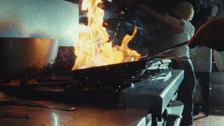 Dramatic super slow motion close up of a chef flambéing a dish in a hot pan in a professional kitchen