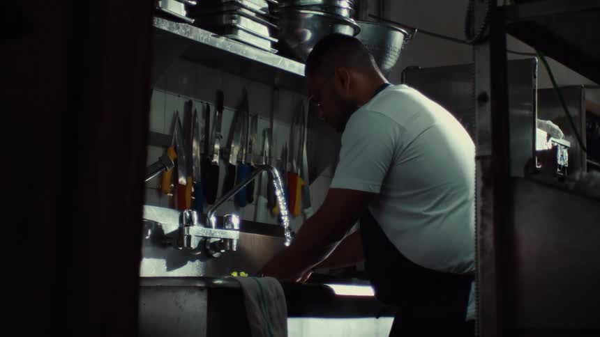 Slow motion shot of a chef washing produce in a stainless steel sink in a dark professional kitchen