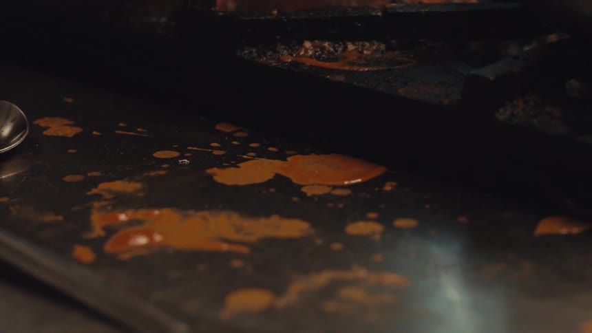 A close-up shot of a messy kitchen counter with spilled sauce being moved around with a spoon