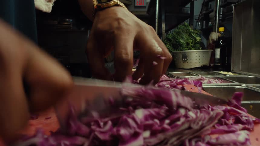 A professional chef rapidly chops fresh red cabbage with a large knife on a cutting board in a restaurant kitchen