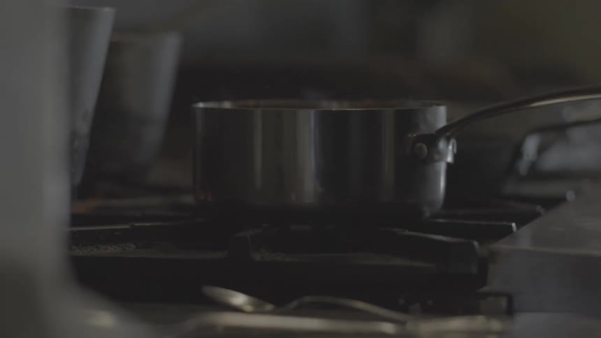 Close up of a chef stirring a simmering sauce in a stainless steel pot on a professional kitchen stove