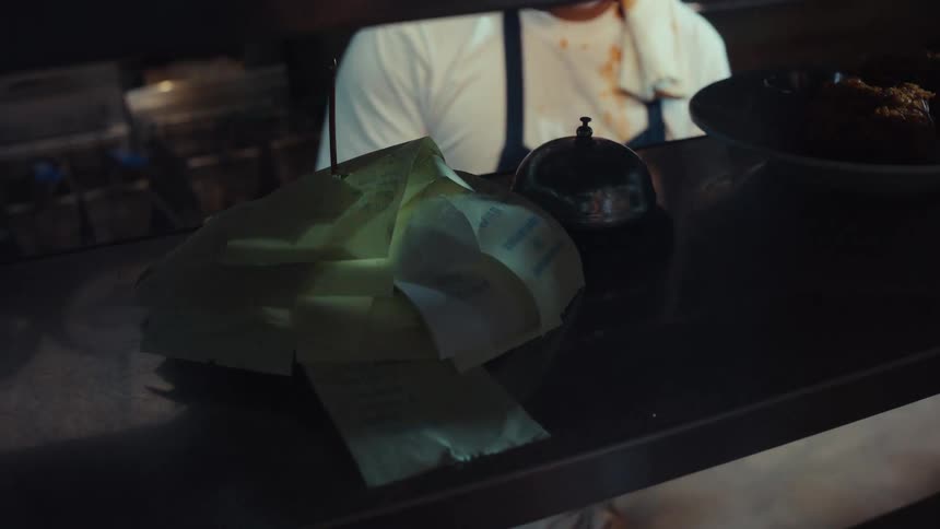 Close up on a chaotic restaurant kitchen order spike during a busy dinner service
