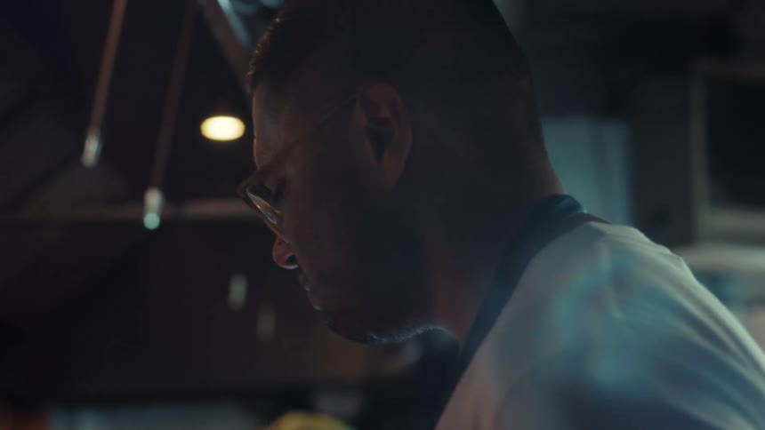 An exhausted chef wipes sweat from his brow after cooking with fire in a hot, professional kitchen in slow motion