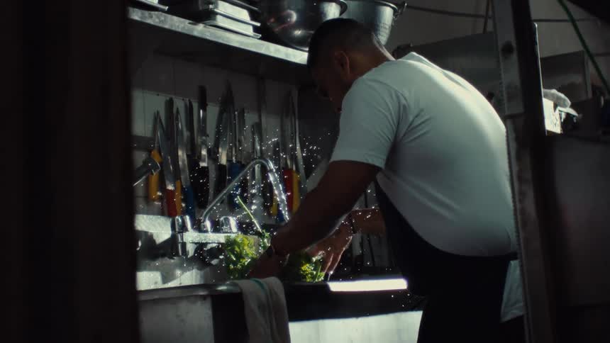 Water splashes in dramatic slow motion as a chef washes fresh leafy greens in a commercial kitchen sink