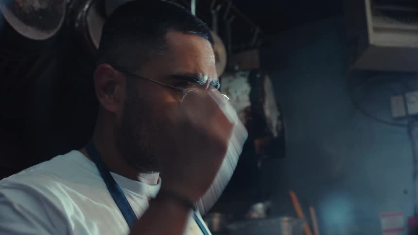 An exhausted chef wipes sweat from his brow while working hard in a hot and steamy professional kitchen