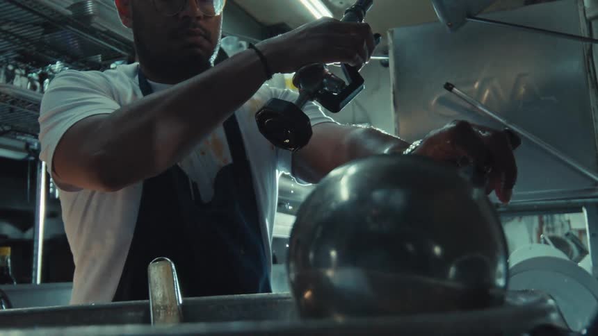 A restaurant worker meticulously cleans a large metal bowl with a spray nozzle in a commercial kitchen, captured in cinematic slow motion