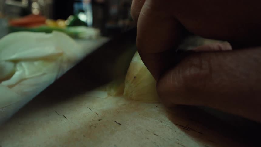 Extreme close-up macro shot of a chef's hands slicing a fresh onion on a cutting board in a professional kitchen