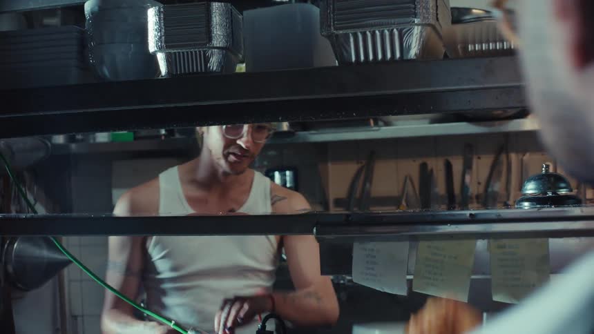 Over-the-shoulder shot of a chef taking a freshly prepared dish from the service pass in a busy restaurant kitchen