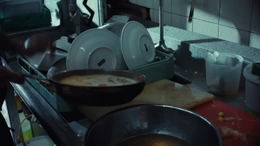 Slow motion shot of a chef cooking a steaming dish in a pan and draining it in a professional kitchen