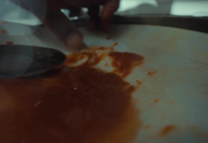 A close-up of a finger wiping leftover sauce from a plate before the dish is washed with water