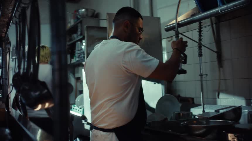 A dishwasher diligently works rinsing dirty plates in a professional restaurant kitchen