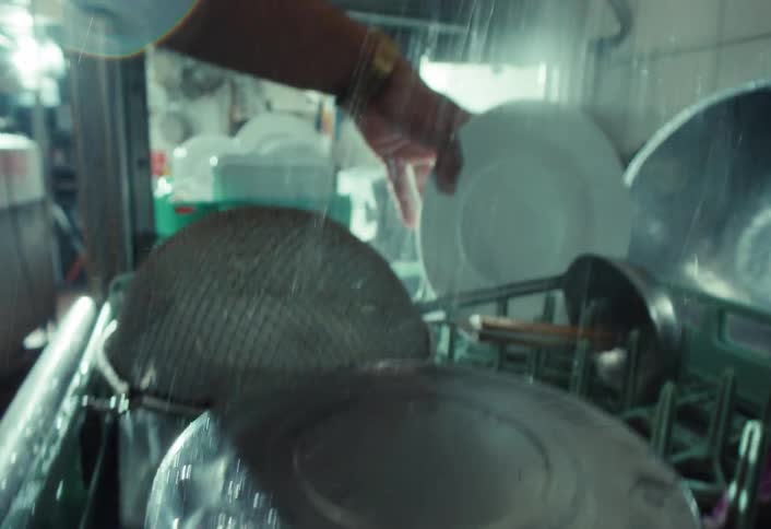 A restaurant worker sprays down a rack of dirty dishes, pots, and pans in a commercial kitchen