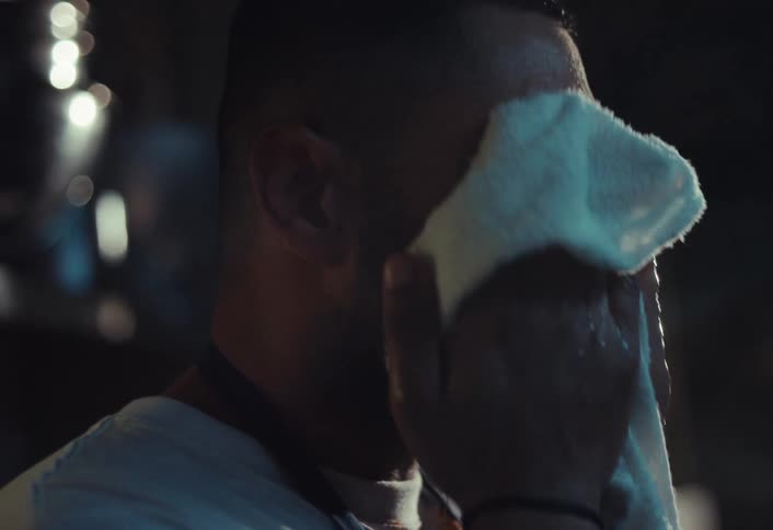 An exhausted chef wipes the sweat from his face with a white towel after a long shift in a hot kitchen