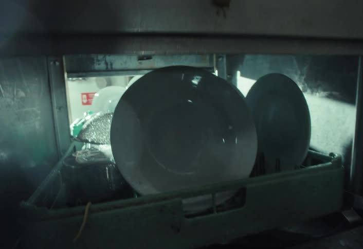 POV shot from inside a large industrial dishwasher as a kitchen worker loads a rack of plates and closes the lid to begin the wash cycle