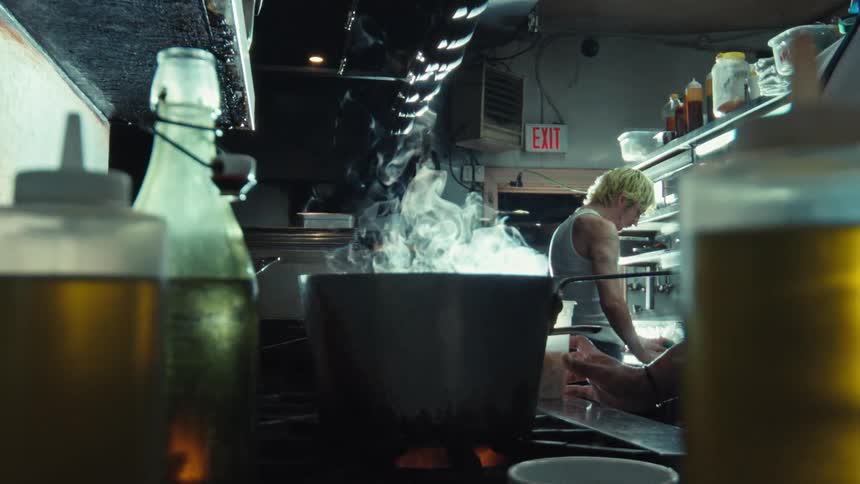 Steam rises in slow motion from a large pot on the stove in a dimly lit professional kitchen