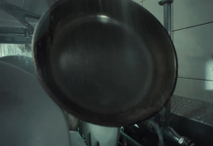 A dishwasher scrapes food from a frying pan and rinses it in a restaurant kitchen sink in dramatic slow motion