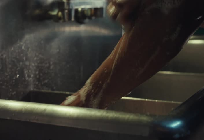Close-up of a man in an apron carefully washing his hands and arms with soap in a kitchen sink