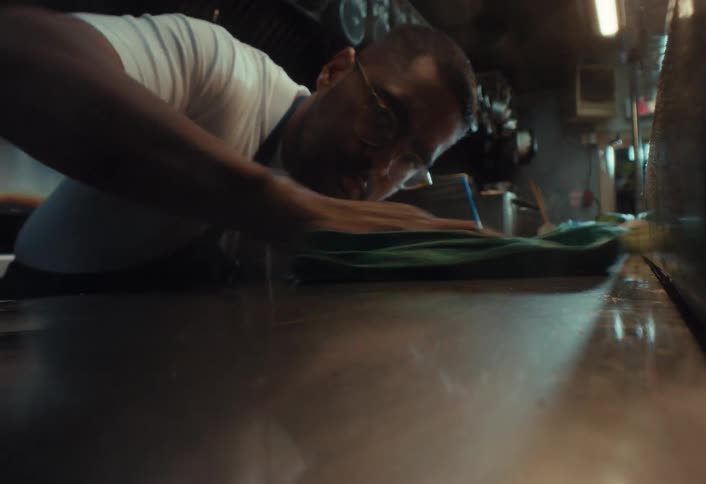 Slow-motion close-up shot of a restaurant worker spraying and wiping down a messy stainless steel countertop