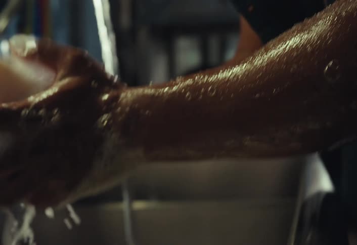 A chef with glasses thoroughly washes his hands and forearms with soap in a commercial kitchen sink