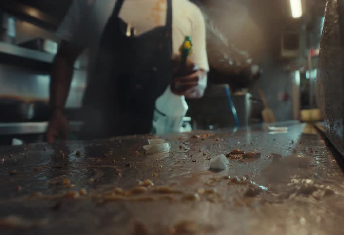 A kitchen worker thoroughly sprays and wipes down a messy stainless steel countertop until it is sparkling clean