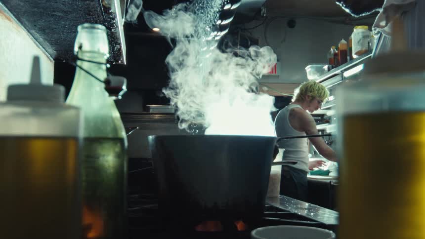 Dramatic slow motion of seasoning being added to a steaming pot on a stove in a professional restaurant kitchen