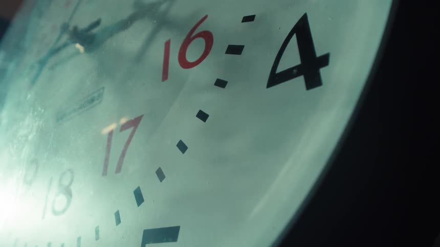 Close up of a large analog clock with red and black numbers as the hands move forward