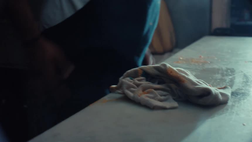 A restaurant worker wipes spilled spaghetti and tomato sauce off a marble countertop with a white cloth