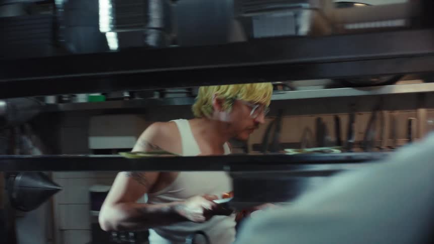Over-the-shoulder shot of a chef taking an order and placing a finished dish on the pass in a bustling restaurant kitchen
