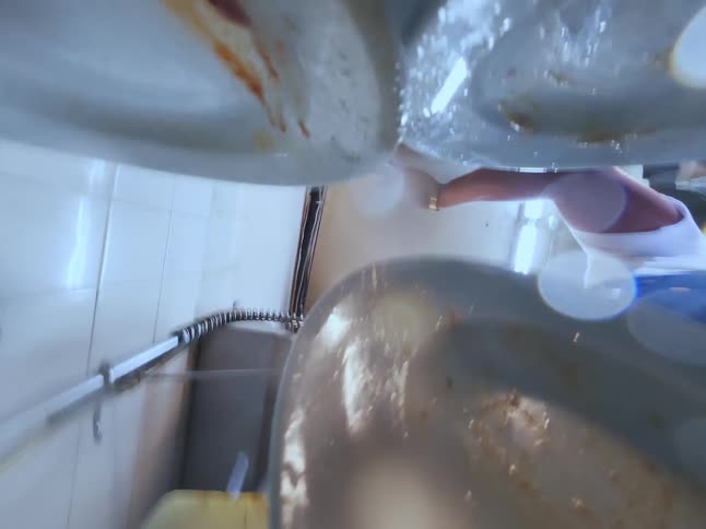 Unique vertical point of view of a man washing dirty dishes with a sprayer in a commercial restaurant kitchen